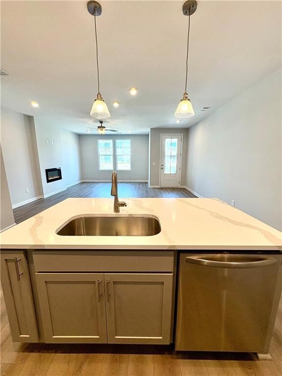 Kitchen with pendant lighting, stainless steel dishwasher, a sink, open floor plan, and a center island with sink