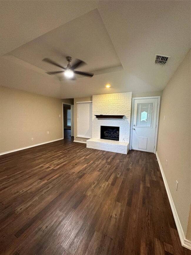 Unfurnished living room featuring dark wood-type flooring, a fireplace, and ceiling fan