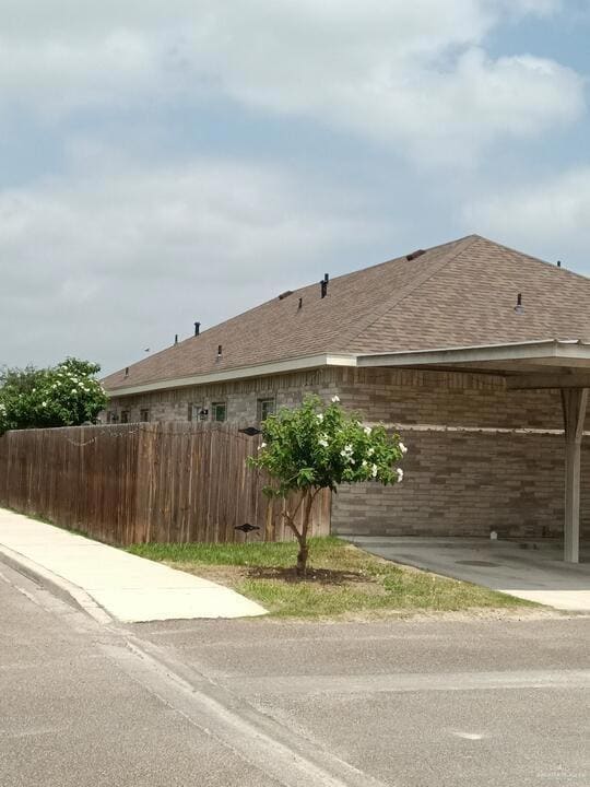 View of side of home featuring a shingled roof and fence