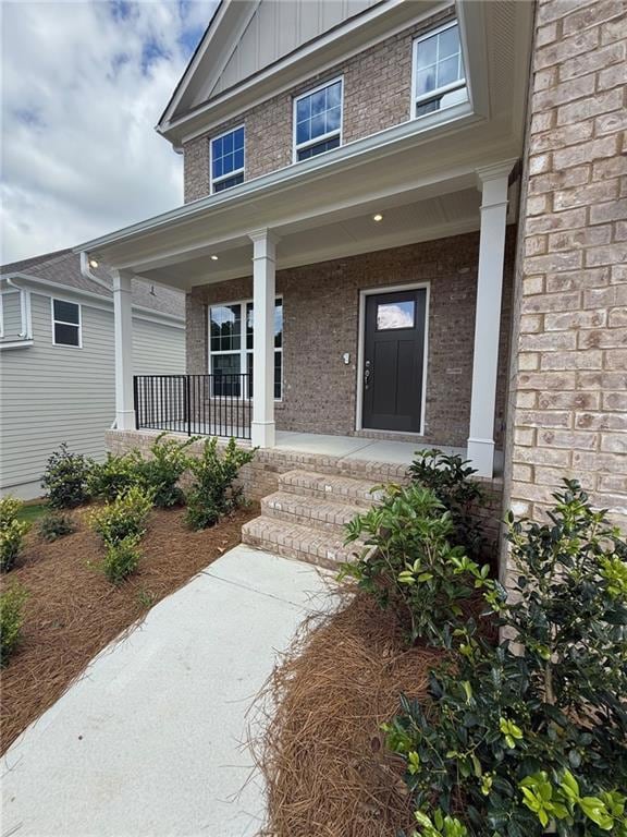 Doorway to property with board and batten siding, brick siding, and a porch