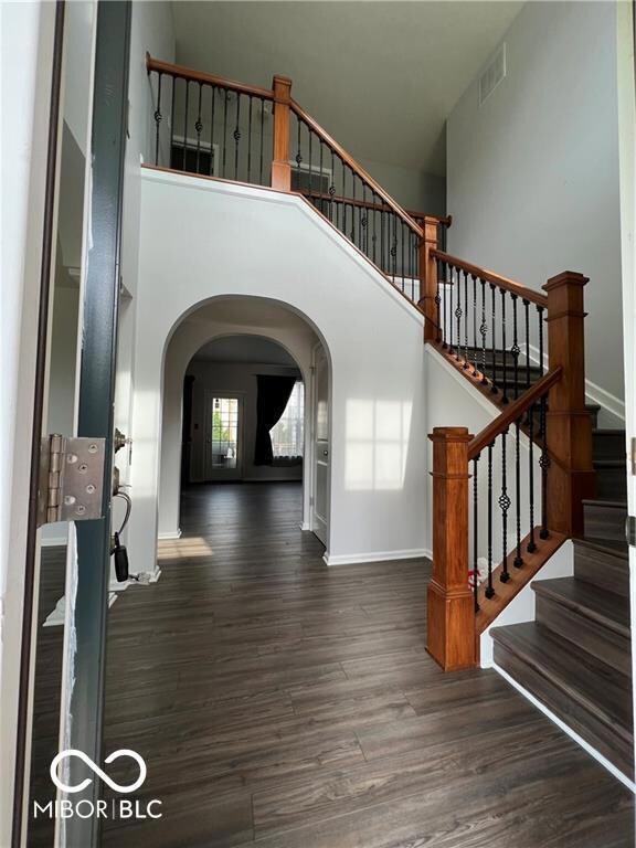foyer entrance featuring a high ceiling, wood finished floors, visible vents, and arched walkways