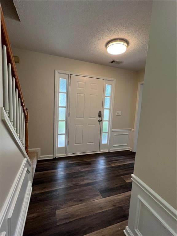 Entryway featuring a textured ceiling, dark wood-style flooring, a wainscoted wall, and stairway