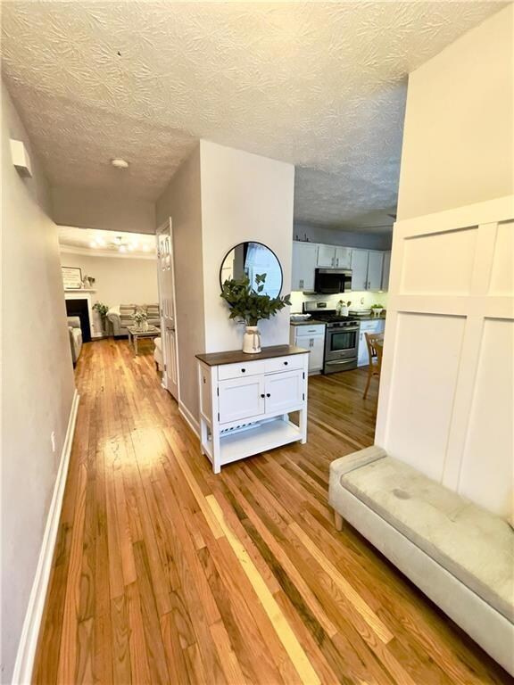 Hall with light wood-type flooring, a textured ceiling, and baseboards