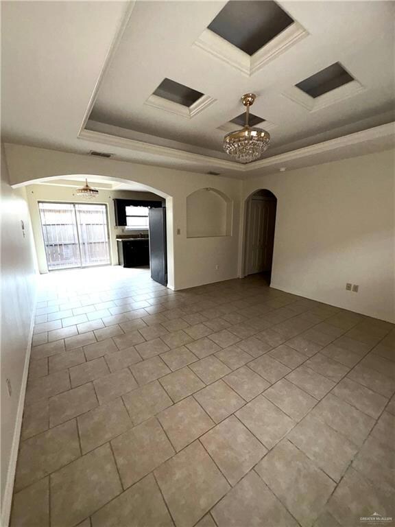 Empty room with visible vents, tile patterned floors, a chandelier, crown molding, and arched walkways