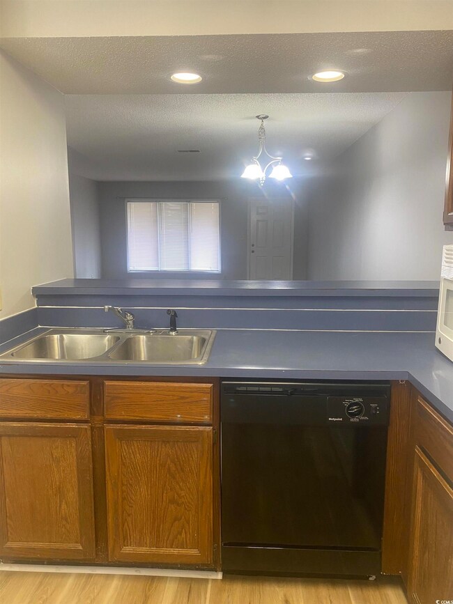 Kitchen featuring black dishwasher, brown cabinets, light wood-type flooring, dark countertops, and white microwave