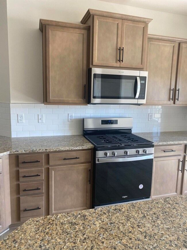 Kitchen with backsplash, appliances with stainless steel finishes, and light stone counters