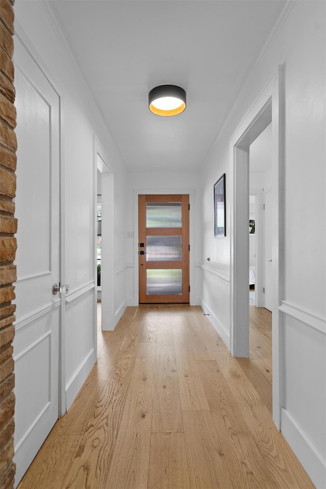 Hallway with light wood finished floors and crown