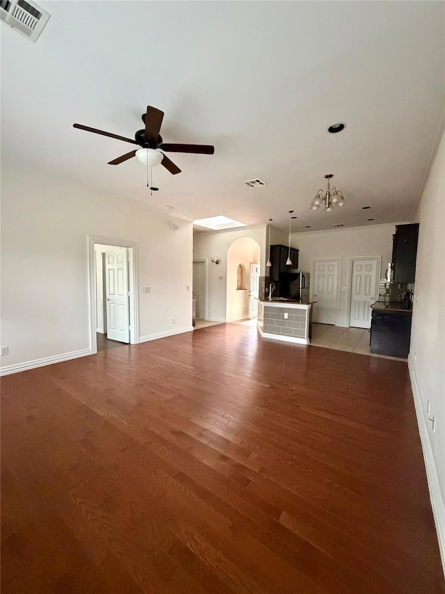 Unfurnished living room featuring arched walkways, dark wood finished floors, and ceiling fan