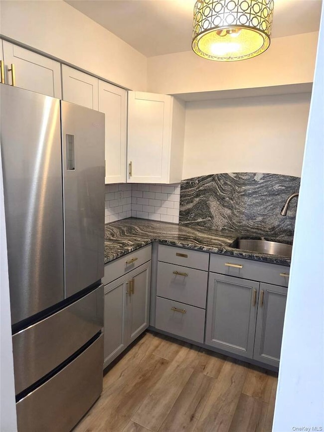 Kitchen featuring gray cabinetry, freestanding refrigerator, light wood-type flooring, dark stone counters, and decorative backsplash