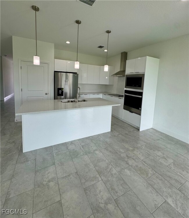 Kitchen featuring white cabinets, hanging light fixtures, appliances with stainless steel finishes, an island with sink, and modern cabinets