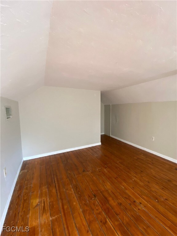 Additional living space featuring vaulted ceiling and dark wood-style flooring