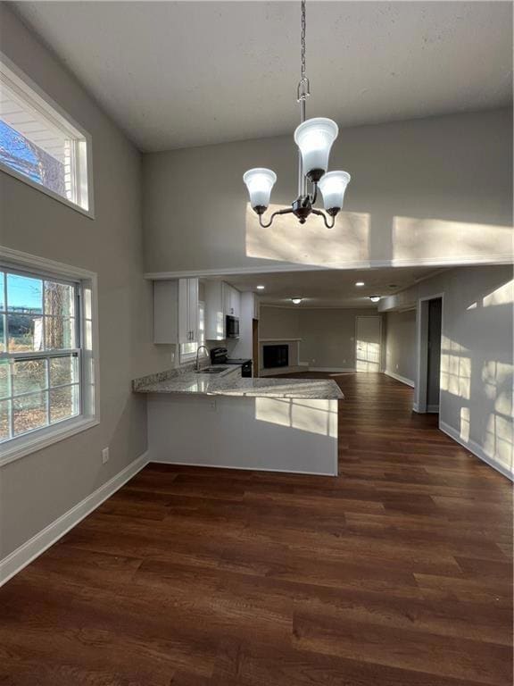 Kitchen with a peninsula, a towering ceiling, a sink, white cabinets, and a chandelier