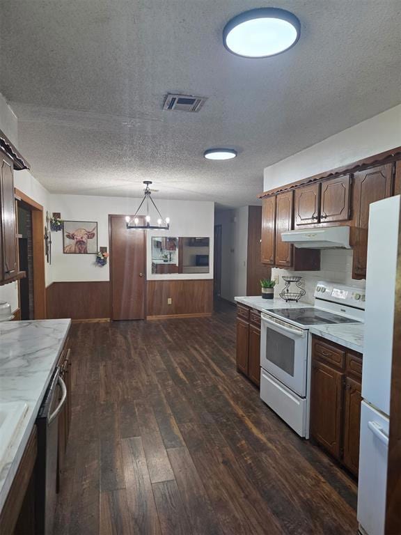 Kitchen with a textured ceiling, white appliances, light countertops, wooden walls, and wainscoting