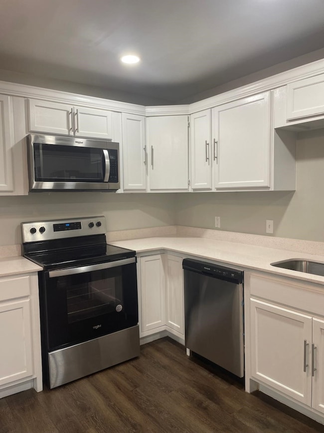 Kitchen featuring appliances with stainless steel finishes, white cabinets, dark wood-style floors, and light stone countertops