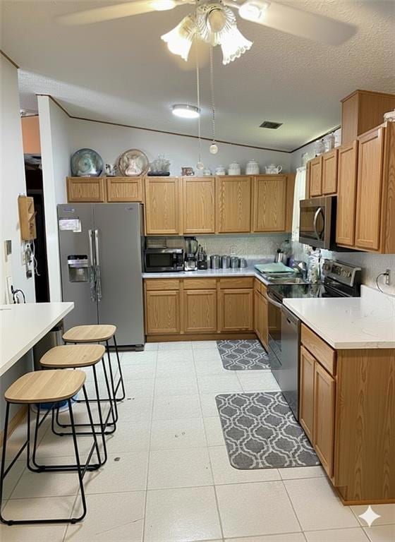 Kitchen with light countertops, stainless steel appliances, a ceiling fan, a textured ceiling, and a kitchen breakfast bar.  Staged Photo.