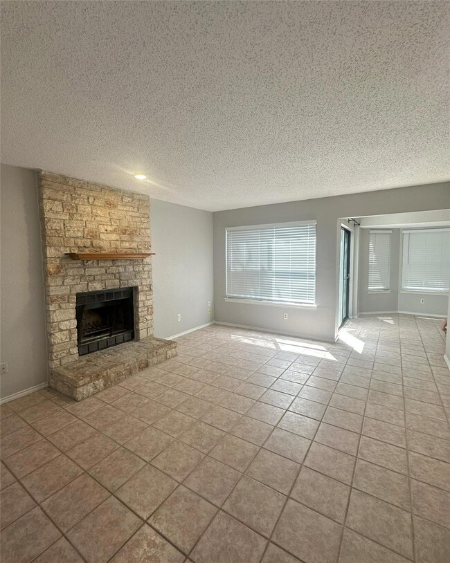 Unfurnished living room featuring tile patterned floors, a stone fireplace, and a textured ceiling
