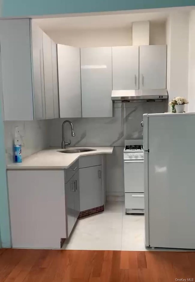 Kitchen with white appliances, under cabinet range hood, light wood-style floors, tasteful backsplash, and gray cabinetry