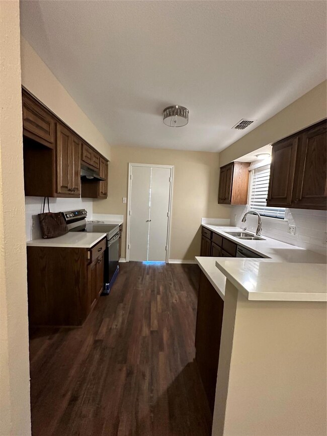 Kitchen featuring extractor fan, dark brown cabinetry, sink, dark hardwood / wood-style floors, and stove