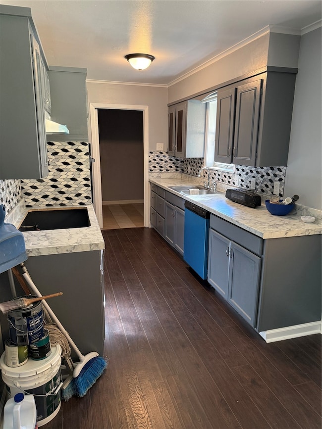 Kitchen with gray cabinetry, light countertops, dark wood-type flooring, tasteful backsplash, and crown molding