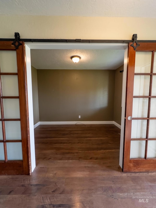 Unfurnished room featuring a barn door, dark wood finished floors, and a textured ceiling