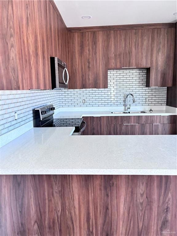 Kitchen with modern cabinets, light stone countertops, range, and tasteful backsplash