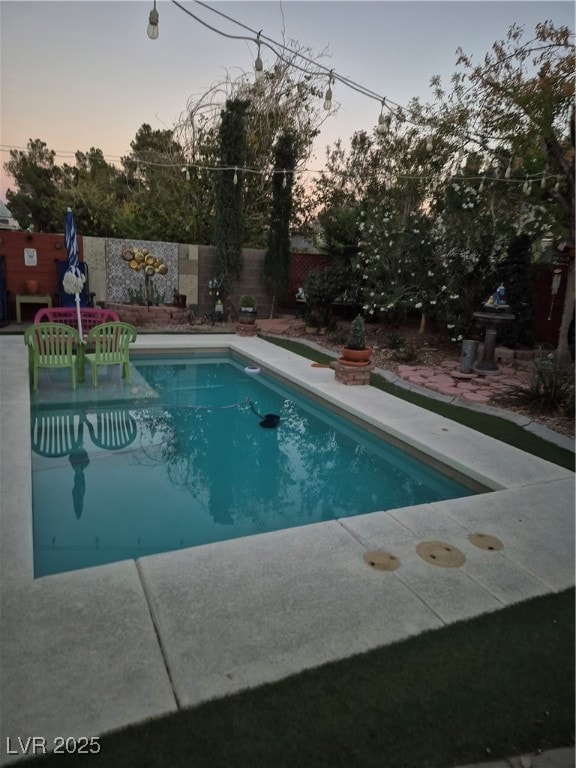 Pool at dusk featuring a fenced backyard and a patio