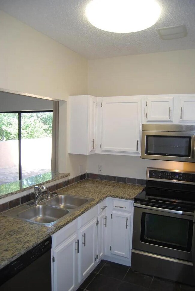 Kitchen featuring stainless steel appliances, white cabinetry, a textured ceiling, and dark tile patterned flooring