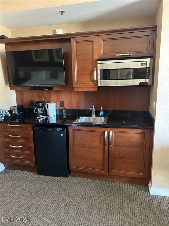 Kitchen with brown cabinetry, stainless steel microwave, black fridge, and dark carpet