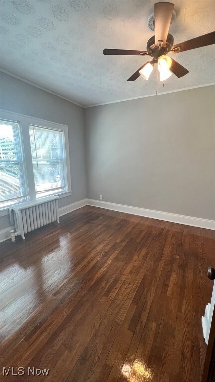 Unfurnished room featuring a textured ceiling, dark wood-style flooring, radiator, crown molding, and a ceiling fan