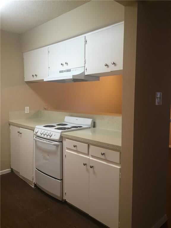 Kitchen with white cabinets, light countertops, white electric stove, under cabinet range hood, and dark wood-style flooring