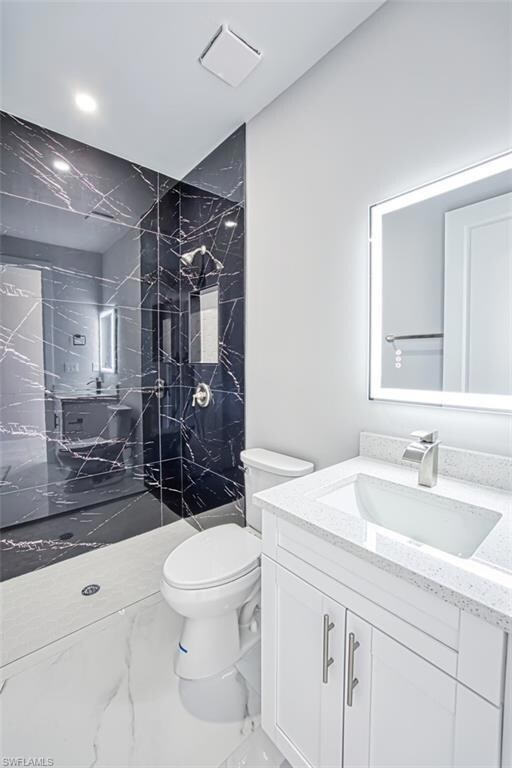 Bathroom featuring toilet, vanity, a marble finish shower, and marble finish flooring