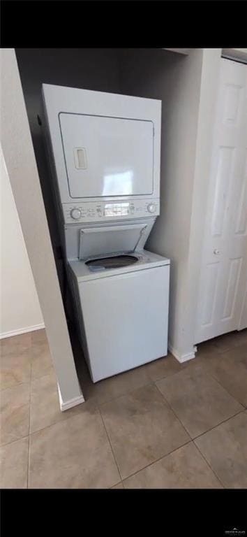 Laundry area featuring stacked washer / drying machine, light tile patterned flooring, and baseboards