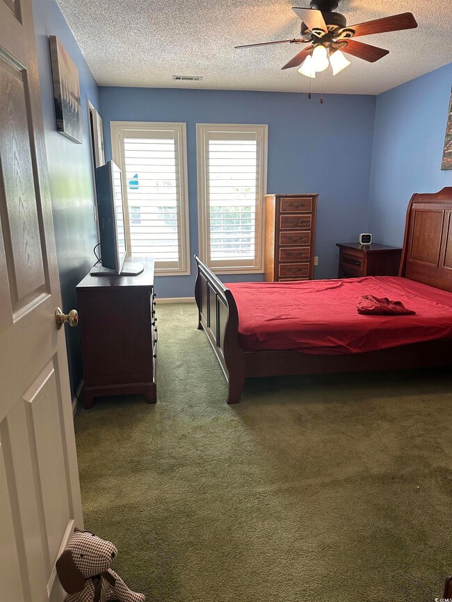 Carpeted bedroom featuring a textured ceiling, ceiling fan, and baseboards