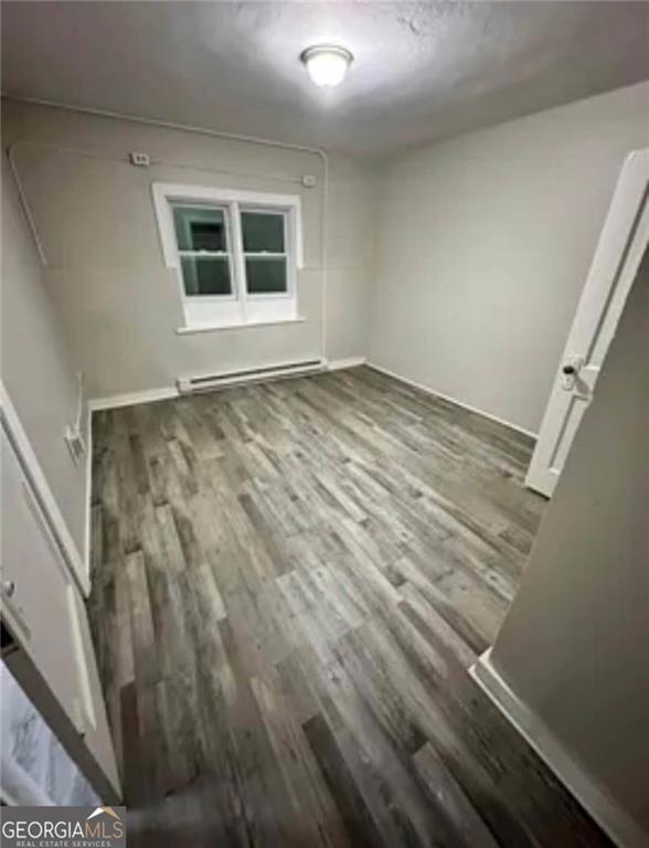 Spare room featuring a baseboard radiator, wood finished floors, and baseboards