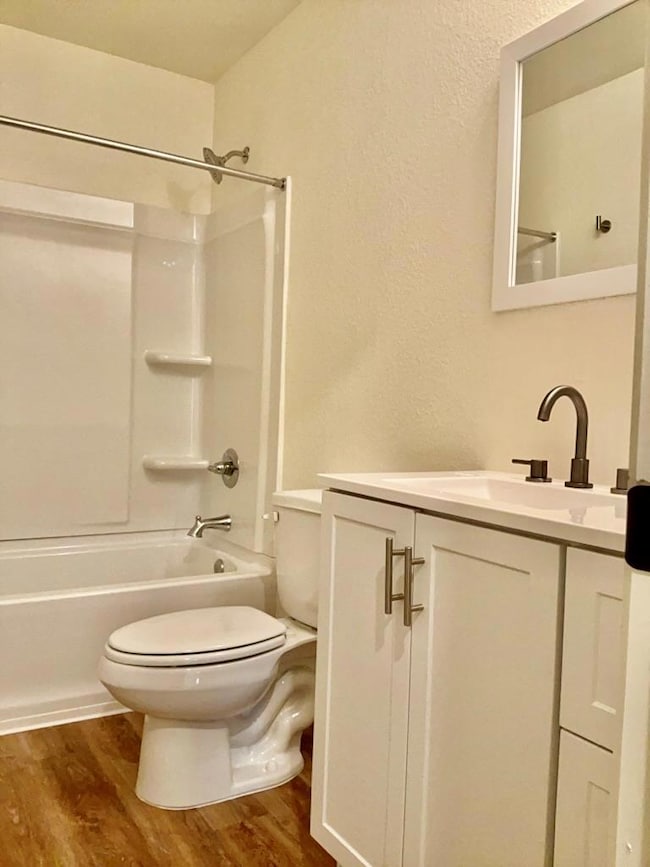 Bathroom with shower / bath combination, vanity, dark wood-style flooring, and a textured wall