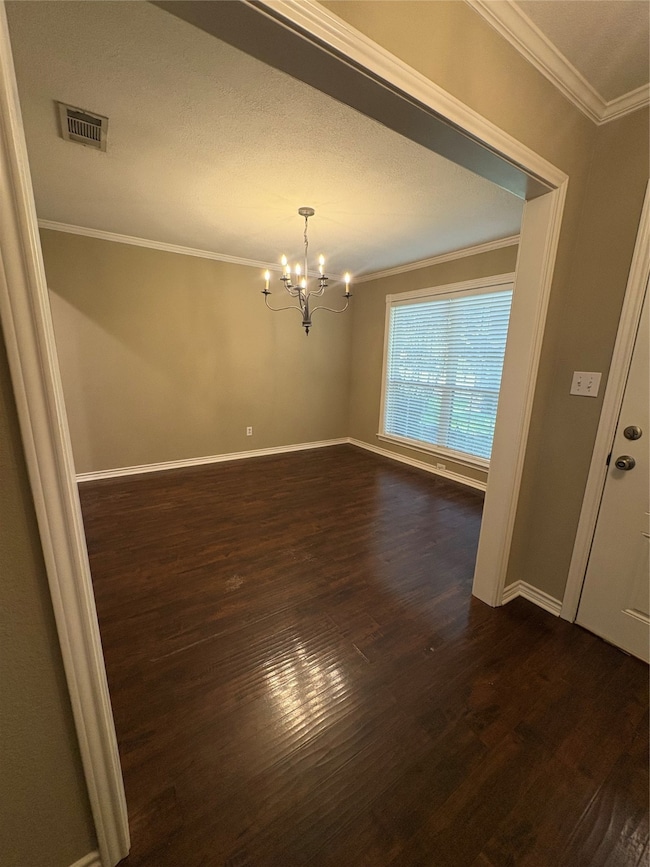 Spare room featuring crown molding, a chandelier, dark wood finished floors, and a textured ceiling