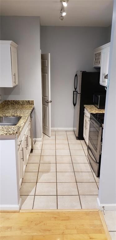 Kitchen with appliances with stainless steel finishes, white cabinetry, light tile patterned flooring, and light stone countertops