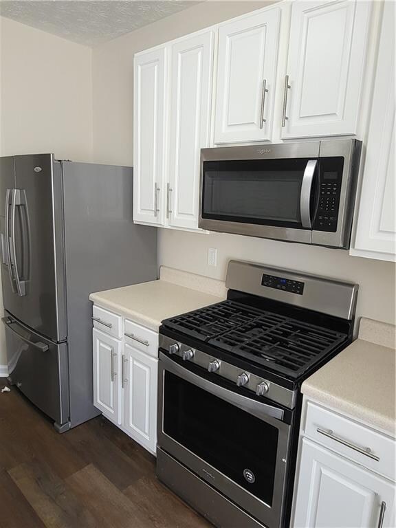 Kitchen featuring appliances with stainless steel finishes, dark wood-style flooring, light countertops, white cabinets, and a textured ceiling