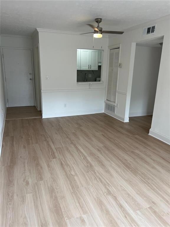 Unfurnished living room featuring a ceiling fan, light wood finished floors, ornamental molding, and baseboards