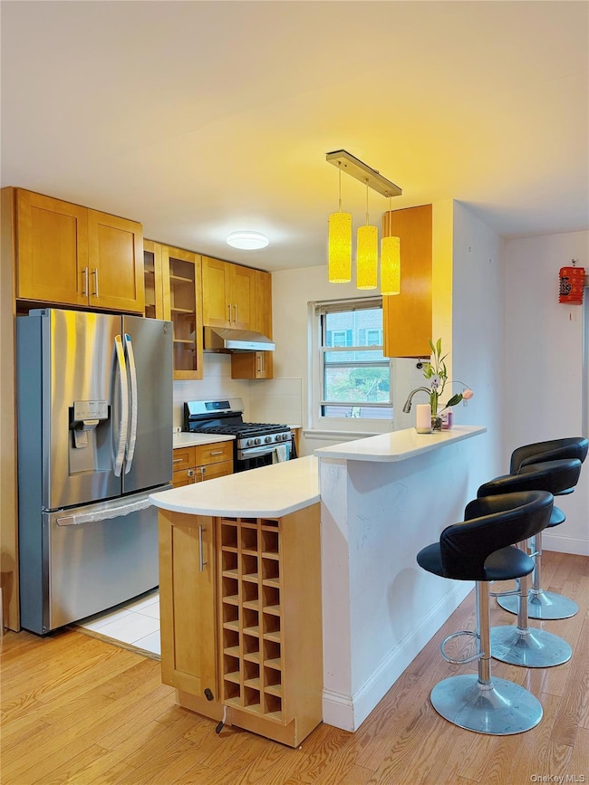 Kitchen with glass insert cabinets, appliances with stainless steel finishes, decorative light fixtures, a peninsula, and light wood-type flooring