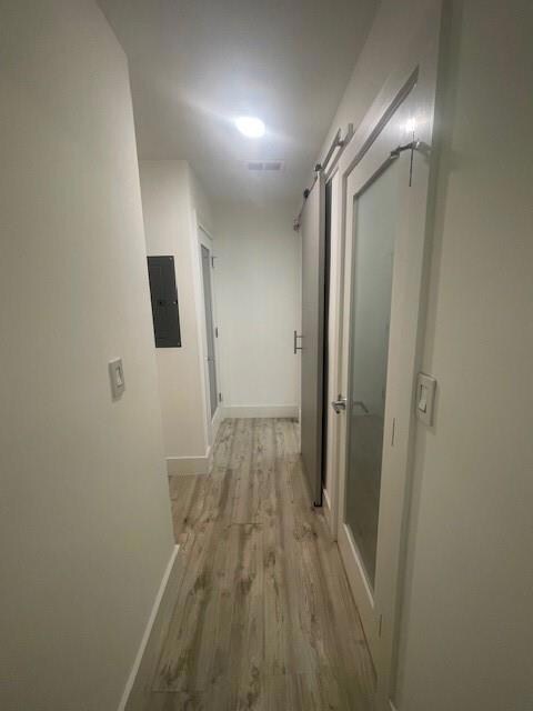 Hall with a barn door, light wood-style flooring, and electric panel