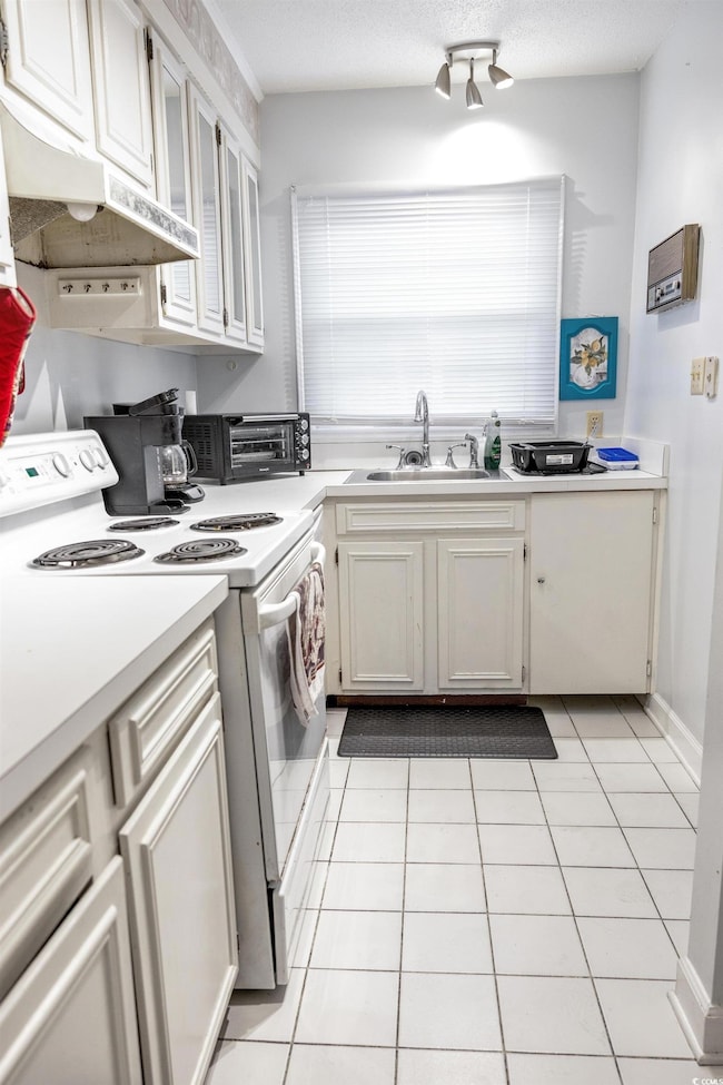 Kitchen featuring white electric stove, a sink, under cabinet range hood, light countertops, and light tile patterned floors