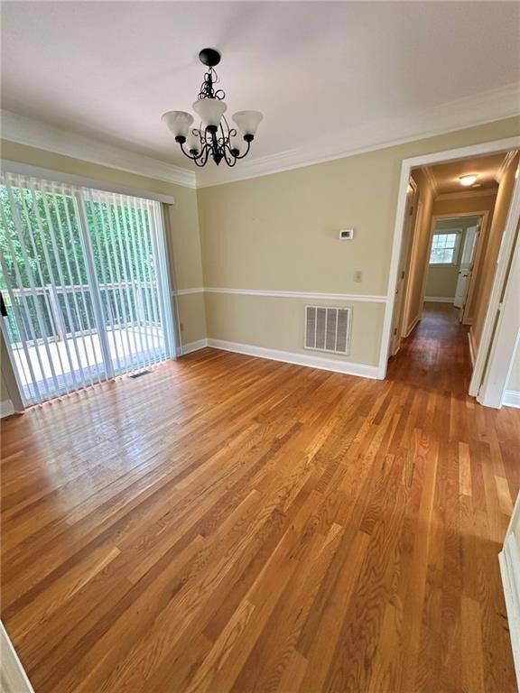 Spare room featuring crown molding, a chandelier, baseboards, and light wood-style floors
