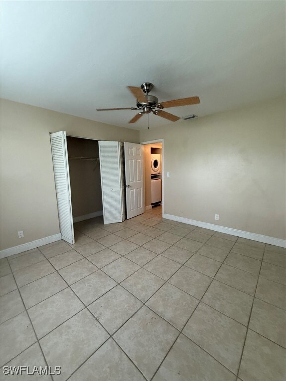 Unfurnished bedroom featuring washer / dryer, a closet, light tile patterned floors, and a ceiling fan