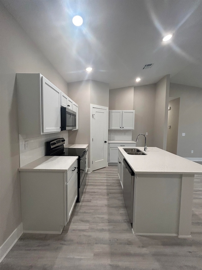 Kitchen featuring stainless steel appliances, light wood-type flooring, an island with sink, recessed lighting, and white cabinetry