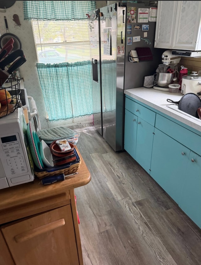 Kitchen with light countertops, blue cabinetry, stainless steel fridge, light wood finished floors, and white microwave