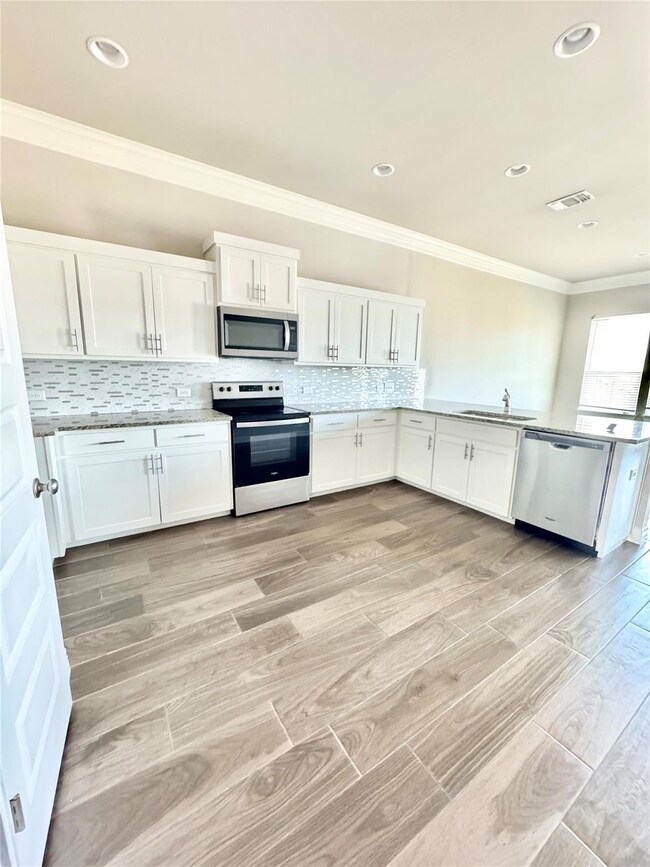 Kitchen with crown molding, white cabinets, stainless steel appliances, decorative backsplash, and light wood-style floors