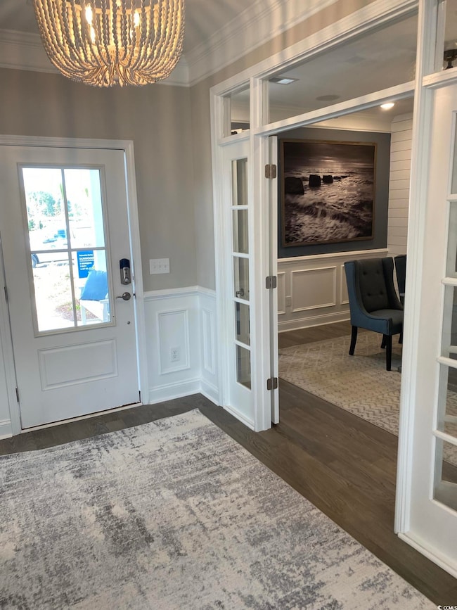 Foyer featuring a chandelier, crown molding, a decorative wall, dark wood-type flooring, and wainscoting