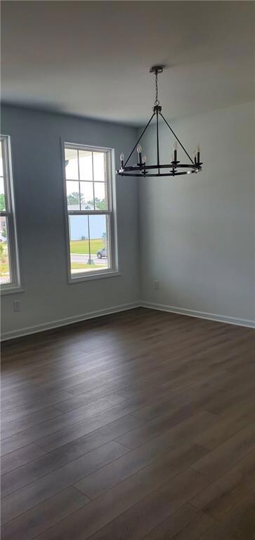 Unfurnished dining area with a chandelier, dark wood finished floors, and healthy amount of natural light