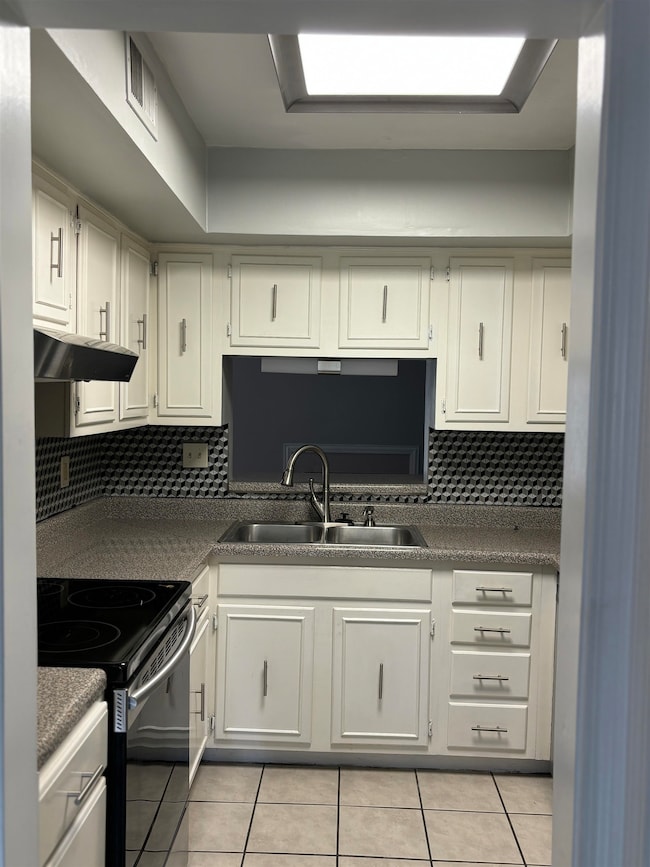 Kitchen featuring range with electric cooktop, light tile patterned floors, a sink, and under cabinet range hood
